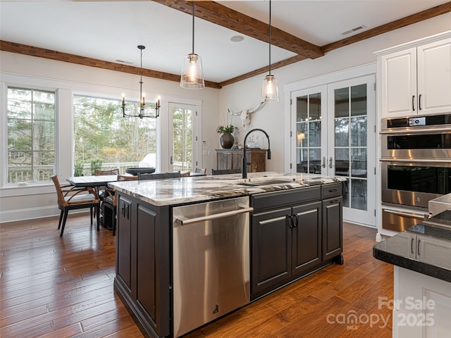 kitchen with stainless steel appliances, white cabinets, french doors, an island with sink, and hanging light fixtures