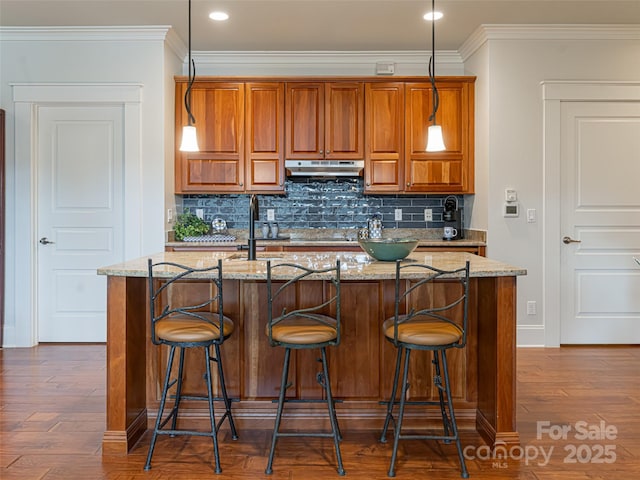 kitchen featuring a kitchen breakfast bar, light stone countertops, dark hardwood / wood-style flooring, pendant lighting, and crown molding