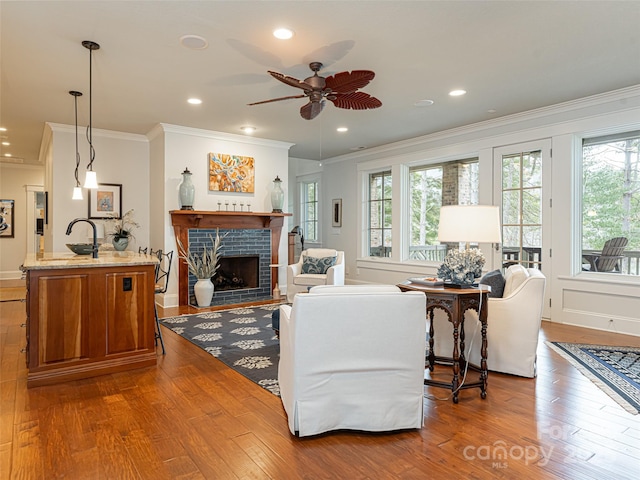 living room featuring a brick fireplace, ceiling fan, hardwood / wood-style flooring, and crown molding