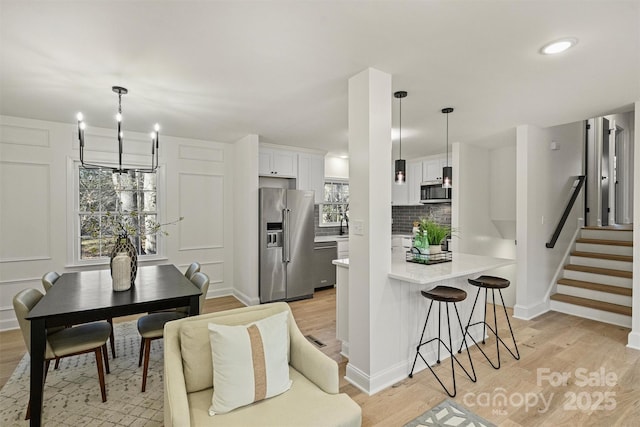 kitchen with appliances with stainless steel finishes, light wood-type flooring, white cabinetry, decorative light fixtures, and tasteful backsplash