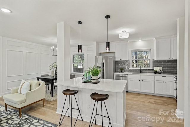 kitchen with appliances with stainless steel finishes, light wood-type flooring, white cabinets, decorative light fixtures, and sink