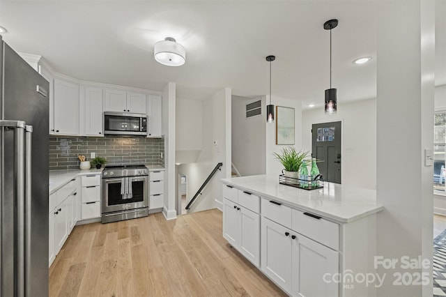 kitchen with stainless steel appliances, white cabinets, decorative light fixtures, light wood-type flooring, and decorative backsplash