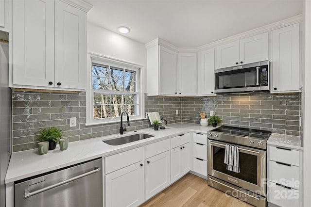 kitchen with stainless steel appliances, white cabinets, sink, and light hardwood / wood-style flooring