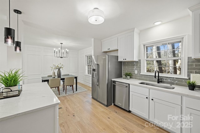 kitchen with appliances with stainless steel finishes, hanging light fixtures, white cabinetry, and sink