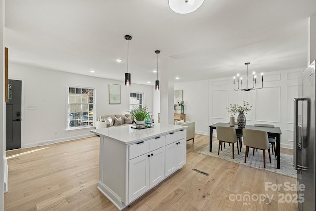 kitchen with light hardwood / wood-style floors, hanging light fixtures, a center island, high quality fridge, and white cabinetry