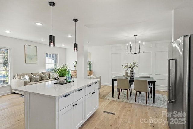 kitchen featuring white cabinets, high quality fridge, light hardwood / wood-style floors, a kitchen island, and pendant lighting