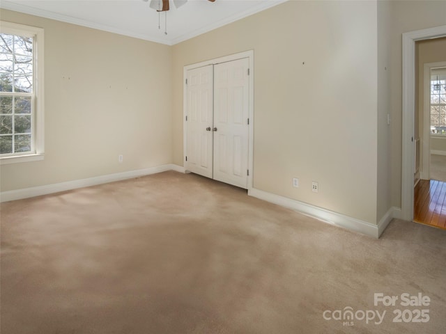 unfurnished bedroom with crown molding, a closet, ceiling fan, and light colored carpet