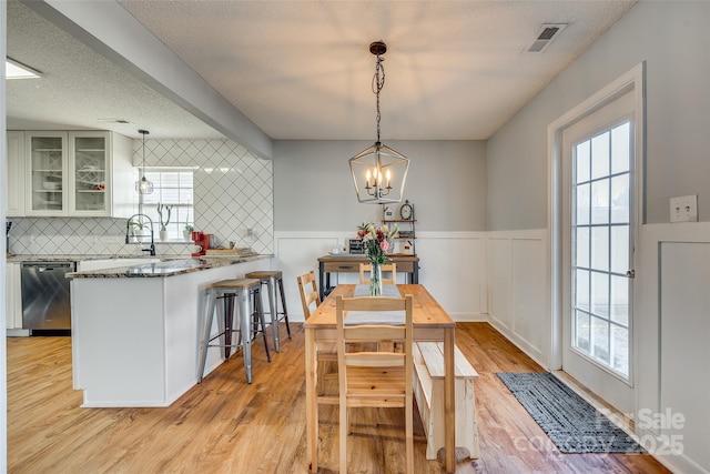 dining space with sink, a textured ceiling, light hardwood / wood-style floors, and a notable chandelier