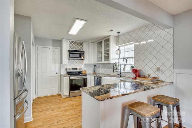 kitchen with sink, white cabinets, dark stone countertops, kitchen peninsula, and appliances with stainless steel finishes