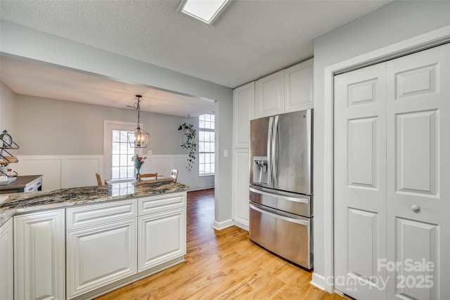 kitchen with dark stone counters, stainless steel refrigerator with ice dispenser, a textured ceiling, white cabinetry, and decorative light fixtures