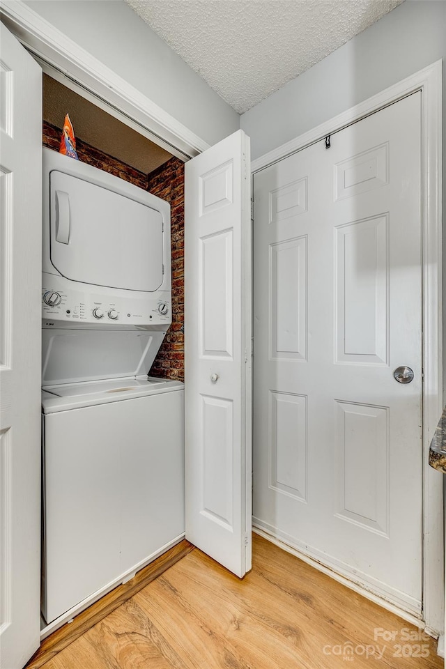 laundry area featuring a textured ceiling, light wood-type flooring, and stacked washer / drying machine