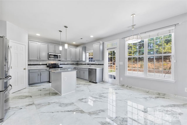 kitchen with decorative light fixtures, gray cabinets, a kitchen island, plenty of natural light, and stainless steel appliances