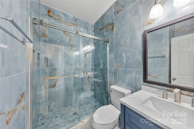 bathroom featuring toilet, a shower with door, vanity, and tile walls