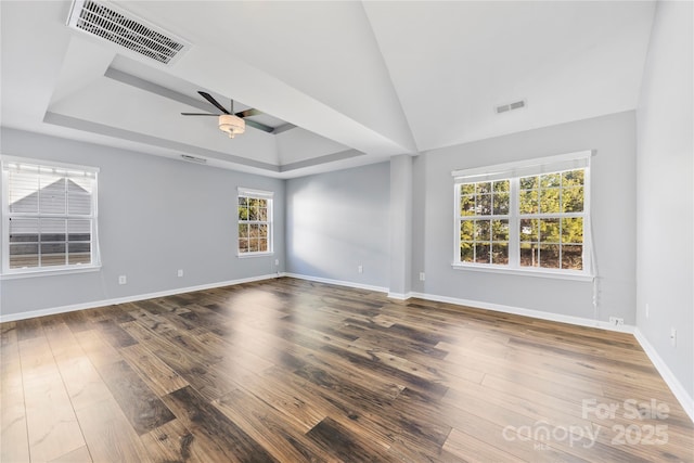 empty room featuring ceiling fan, a healthy amount of sunlight, a raised ceiling, and hardwood / wood-style flooring