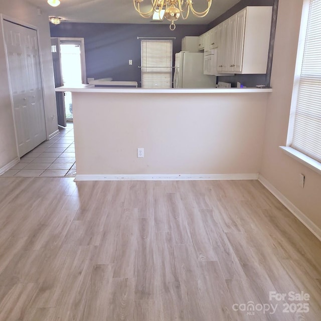 kitchen featuring white cabinetry, a chandelier, white fridge, kitchen peninsula, and light hardwood / wood-style flooring