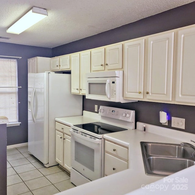 kitchen with sink, white appliances, light tile patterned floors, and a textured ceiling