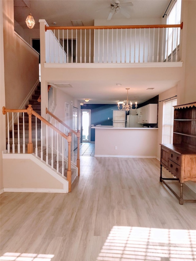 unfurnished living room featuring a high ceiling, ceiling fan with notable chandelier, and light hardwood / wood-style floors