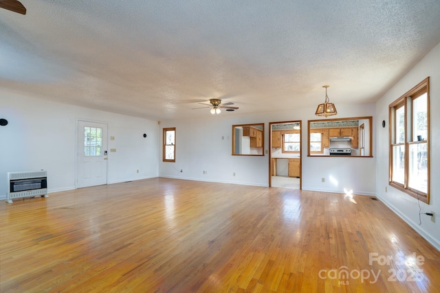 unfurnished living room with heating unit, ceiling fan with notable chandelier, a textured ceiling, and light hardwood / wood-style floors