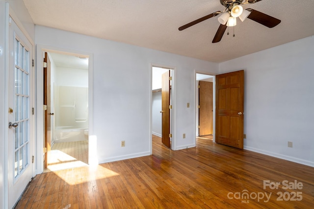 unfurnished bedroom featuring a spacious closet, hardwood / wood-style floors, a closet, ceiling fan, and ensuite bathroom