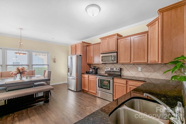 kitchen featuring pendant lighting, crown molding, dark countertops, appliances with stainless steel finishes, and a sink