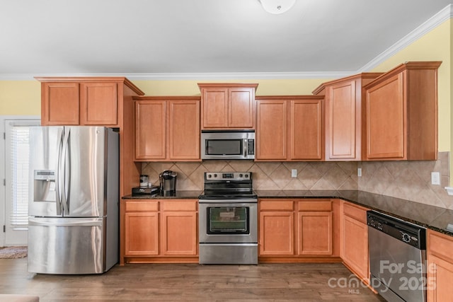 kitchen featuring ornamental molding, appliances with stainless steel finishes, tasteful backsplash, dark stone countertops, and dark wood finished floors