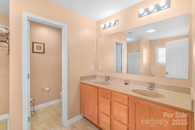 bathroom featuring toilet, double vanity, baseboards, and a sink