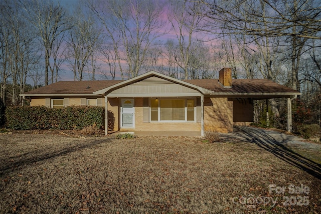 ranch-style house featuring a carport, a porch, and a lawn