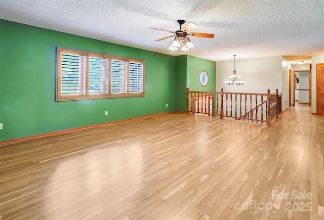 spare room with ceiling fan with notable chandelier, light hardwood / wood-style floors, and a textured ceiling