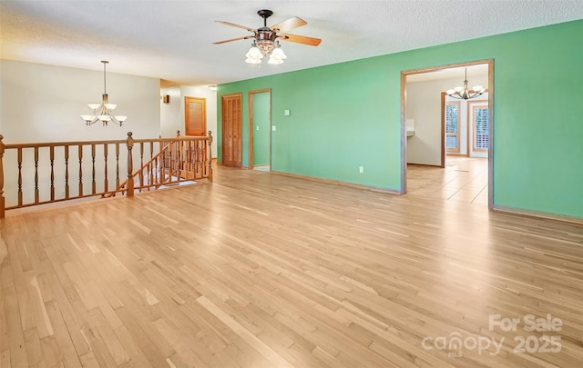 spare room with ceiling fan with notable chandelier, a textured ceiling, and light hardwood / wood-style flooring