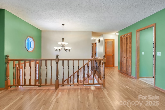 hallway featuring a textured ceiling, light hardwood / wood-style flooring, and a notable chandelier