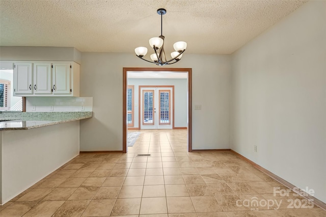 unfurnished dining area featuring french doors, a healthy amount of sunlight, light tile patterned floors, and a notable chandelier