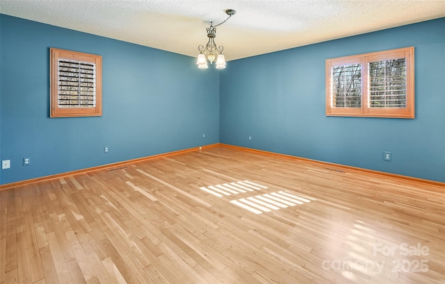 spare room featuring a chandelier, hardwood / wood-style floors, and a textured ceiling