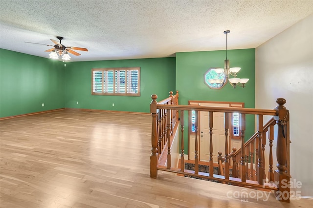 stairs featuring hardwood / wood-style floors, ceiling fan with notable chandelier, and a textured ceiling