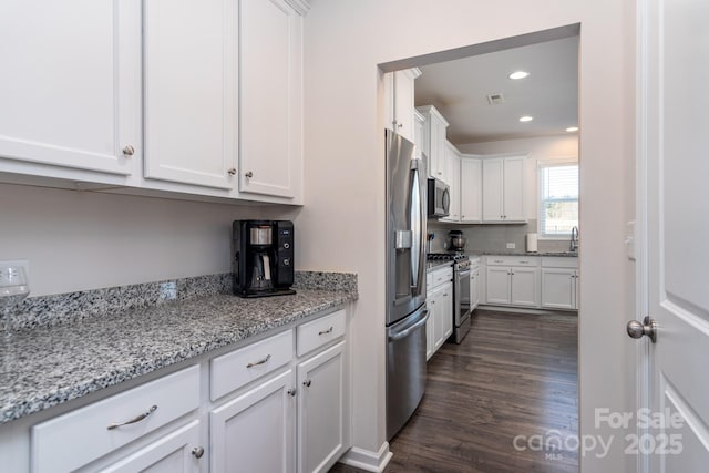 kitchen featuring light stone countertops, appliances with stainless steel finishes, white cabinetry, dark hardwood / wood-style flooring, and sink