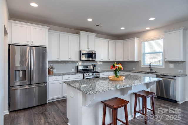 kitchen featuring stainless steel appliances, white cabinets, a kitchen island, and light stone countertops