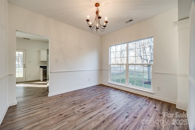 unfurnished room with a wealth of natural light, hardwood / wood-style floors, and a chandelier