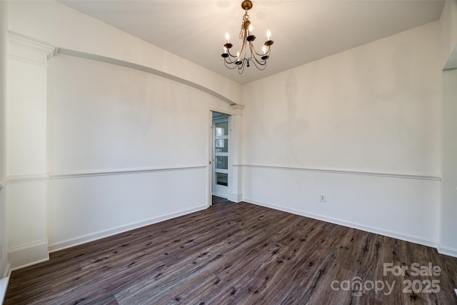 spare room with dark hardwood / wood-style floors and a notable chandelier