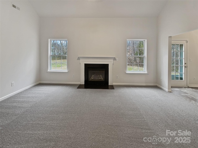 unfurnished living room featuring vaulted ceiling, a wealth of natural light, and carpet flooring