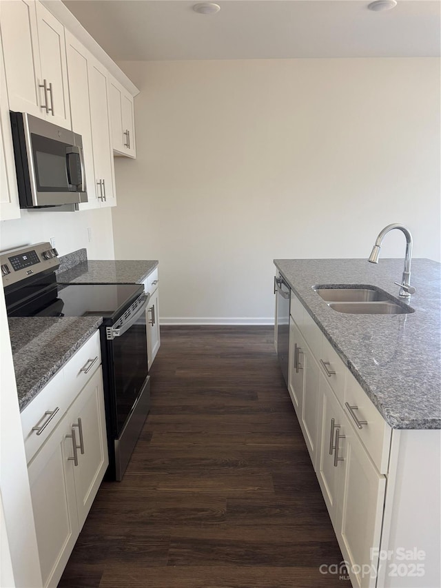 kitchen with appliances with stainless steel finishes, stone countertops, a sink, and dark wood finished floors