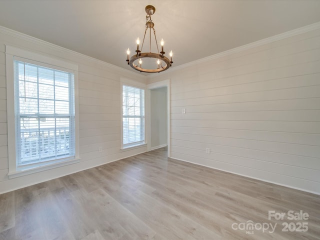 empty room with a notable chandelier, ornamental molding, and light hardwood / wood-style floors