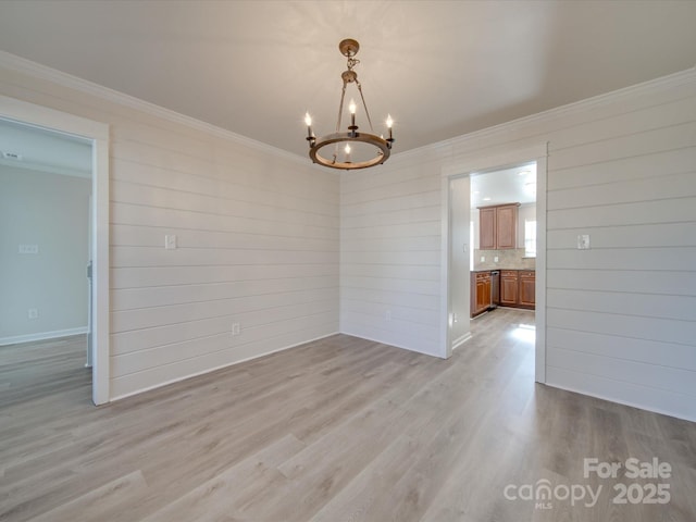 empty room featuring ornamental molding, a notable chandelier, and light wood-type flooring