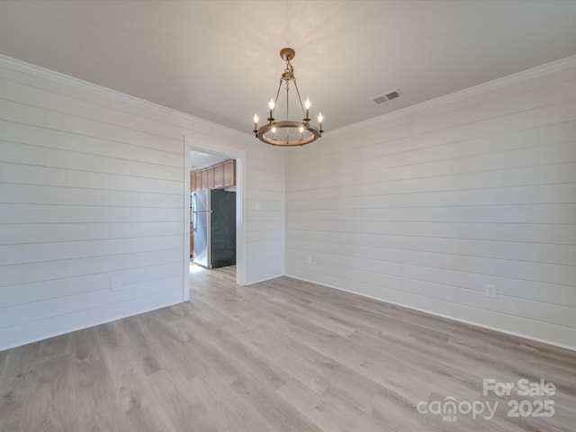 spare room with ornamental molding, an inviting chandelier, and light hardwood / wood-style flooring