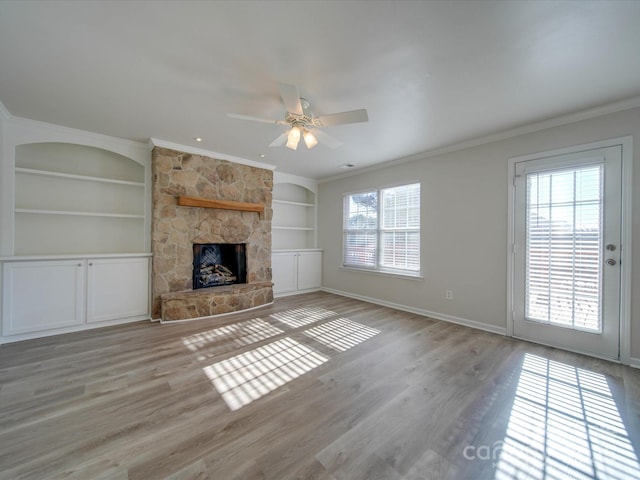 unfurnished living room featuring crown molding, a stone fireplace, and built in features