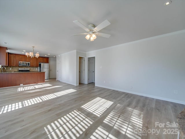 unfurnished living room featuring crown molding, sink, ceiling fan with notable chandelier, and light hardwood / wood-style flooring