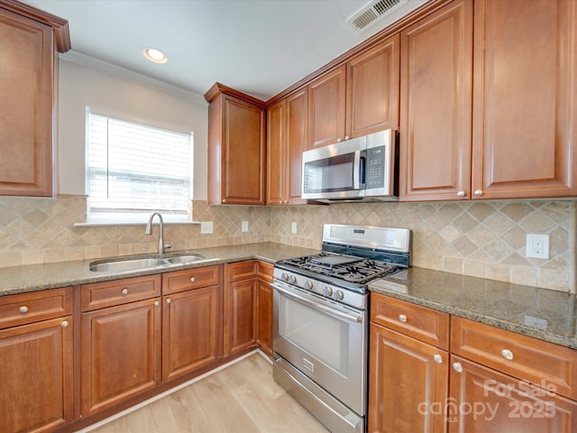 kitchen with stone countertops, sink, ornamental molding, stainless steel appliances, and light hardwood / wood-style flooring