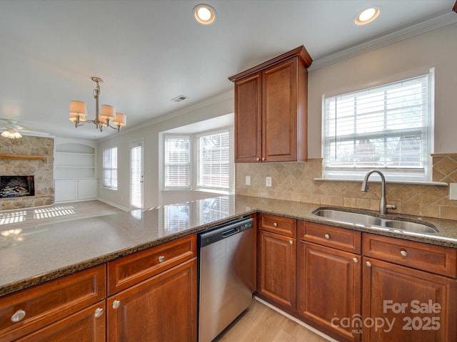 kitchen with ornamental molding, a stone fireplace, sink, and stainless steel dishwasher