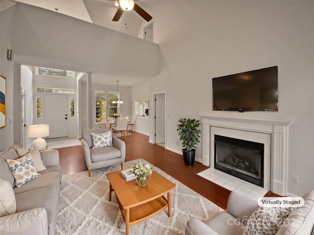 living room with a towering ceiling, a tile fireplace, ceiling fan, and hardwood / wood-style flooring