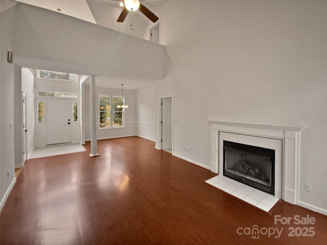 unfurnished living room with a tiled fireplace, ceiling fan, hardwood / wood-style floors, and high vaulted ceiling