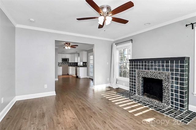 unfurnished living room featuring ceiling fan, a tiled fireplace, ornamental molding, and wood-type flooring