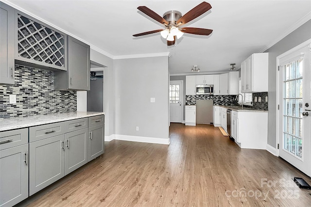 kitchen with appliances with stainless steel finishes, white cabinetry, tasteful backsplash, gray cabinets, and crown molding